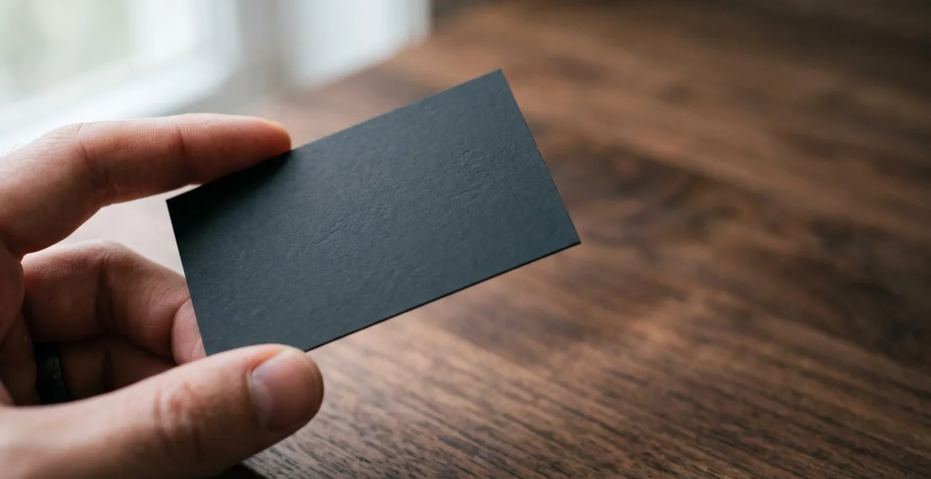 Carte de visite noire au pelliculage mat tenue délicatement entre deux doigts, illustrant un rendu premium et discret