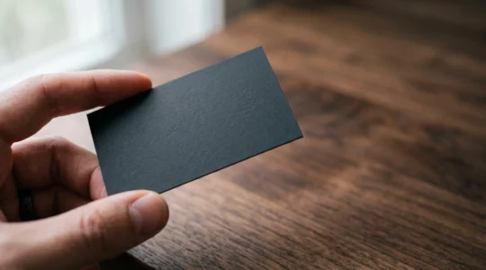 Carte de visite noire au pelliculage mat tenue délicatement entre deux doigts, illustrant un rendu premium et discret