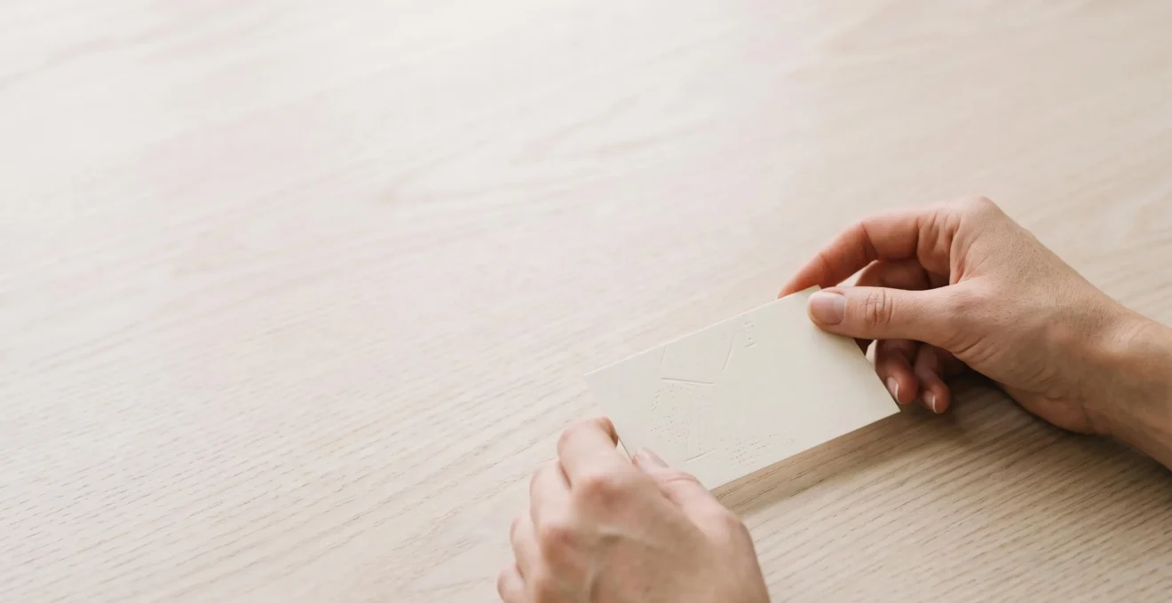 Carte d'invitation minimaliste posée sur une table en bois clair, avec un espace négatif dominant et une lumière douce