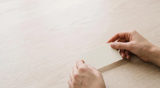 Carte d'invitation minimaliste posée sur une table en bois clair, avec un espace négatif dominant et une lumière douce
